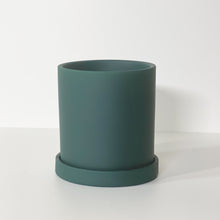 Load image into Gallery viewer, The Cyn is a forest green cylinder-shaped planter pot. The planter pot has a drainage hole and a saucer that helps catch water.
