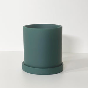 The Cyn is a forest green cylinder-shaped planter pot. The planter pot has a drainage hole and a saucer that helps catch water.