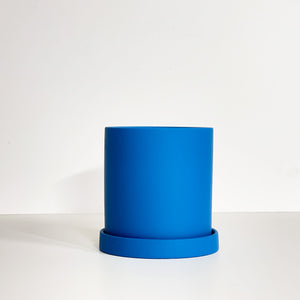 The Cyn is a midnight blue cylinder-shaped planter pot. The planter pot has a drainage hole and a saucer that helps catch water.
