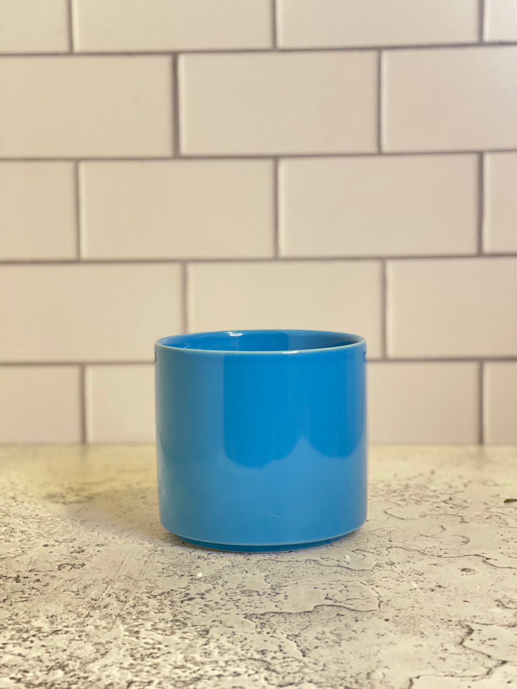 A bright blue cylinder-shaped planter pot with a glossy finish. The planter pot includes a drainage hole.