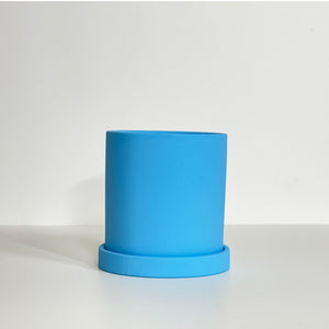 The Cyn is a sky blue cylinder-shaped planter pot. The planter pot has a drainage hole and a saucer that helps catch water.