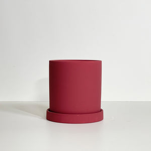 The Cyn is a burgundy color cylinder-shaped planter pot. The planter pot has a drainage hole and a saucer that helps catch water.
