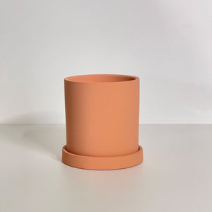 The Cyn is a taupe cylinder-shaped planter pot. The planter pot has a drainage hole and a saucer that helps catch water.