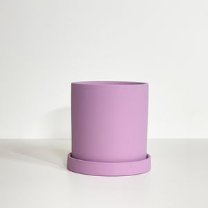 The Cyn is a purple lavender cylinder-shaped planter pot. The planter pot has a drainage hole and a saucer that helps catch water.