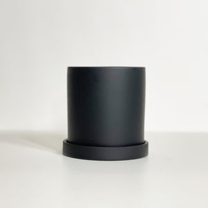 The Cyn is a black cylinder-shaped planter pot. The planter pot has a drainage hole and a saucer that helps catch water.