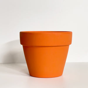 An orange terracotta pot with a matte finish. The planter pot includes a drainage hole.