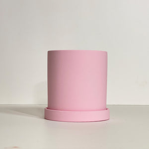 The Cyn is a baby pink cylinder-shaped planter pot. The planter pot has a drainage hole and a saucer that helps catch water.