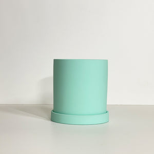 The Cyn is a mint color cylinder-shaped planter pot. The planter pot has a drainage hole and a saucer that helps catch water.